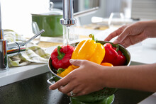 Close-up Of Woman Rinsing Yellow And Red Peppers In Sink