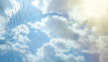 Broken Glass Against A Background Of Blue Sky With Rays Of The Sun. Cracks On The Window Glass. Not A Peaceful Sky.