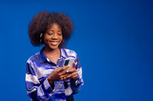 Young Woman Isolated On Blue Background Smiling Using Her Mobile