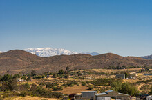 Temecula, CA, USA - April 23, 2022: Snow Covered Eastern Part Of San Jacinto Mountains Viewed From Rural Area North Of Temecula Under Blue Sky, With Brown Hills And Ranches Up Front.