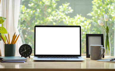 Wall Mural - Laptop computer with blank display, coffee cup, pencil holder and picture frame on wooden table in bright living room.