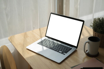 Wall Mural - Computer laptop, coffee cup, notebook and potted plant on wooden table in bright living room.