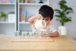 © Sukjai Photo - Blurred of 3 years old asian little boy pouring the water to the cup in montessori class, concept of homeschool, practical life skill, kid learning activity, freedom, education for kid development.