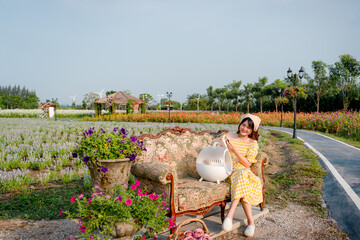 Wall Mural - Cheerful pretty young woman with hair tied by handkerchief reading a book with cute small prairie dog sitting on vintage sofa relaxing in beautiful flower garden. Asian people.