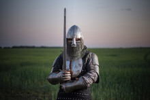 Knight Guardian Armor With A Sword In Hands Stands In The Field On A Sunset Background. The Kingdom Defender Concept.