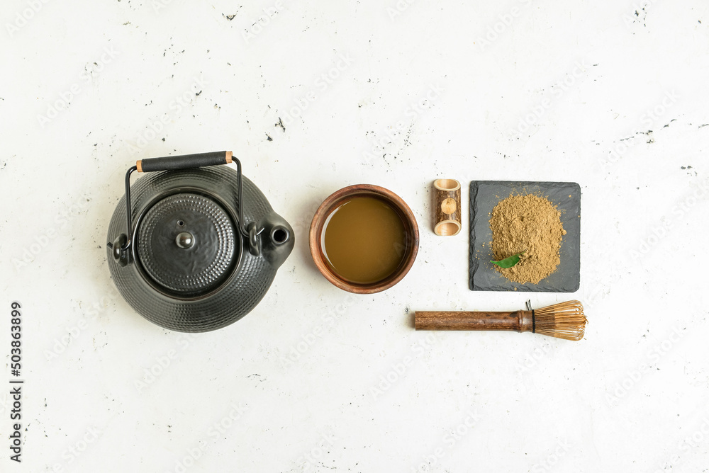 Composition with teapot, chasen, powdered matcha tea and cup of beverage on light background