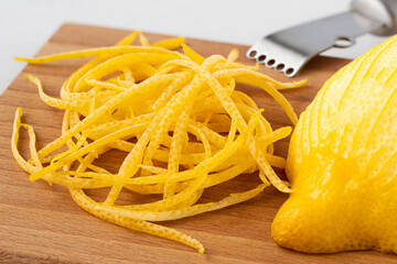 Poster - Heap of peeled lemon zest on wood chopping board next to half of peeled lemon and zester.