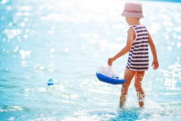 Wall Mural - Little boy playing on the sea beach with toy ship