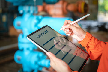 Action of a human is using digital pen to perform checklist on tablet with background of factory workplace. Industrial and technology working concept. Close-up and selective focus at hand's part.