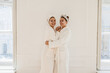 © Look! - Beautiful young caucasian ladies use hydrogel patches while standing hugging on white background. Women wear robes and headbands. Skin care and hydration concept