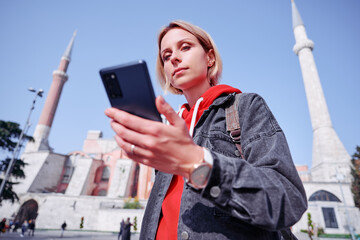 Wall Mural - Enjoying vacation in Istanbul. Young traveling woman using smartphone near Hagia Sophia Temple.