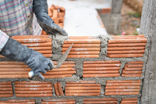 Construction Worker Installing Bricks Masonry Bricklayer And Adjusting Bricks Walls Using Trowel, Mortar And Putty Knife.