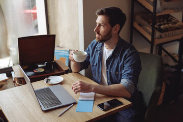 Wall Mural - Thoughtful Caucasian handsome man resting in cafe and working at laptop. Coffee break. Top view.