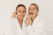 © Look! - Two funny caucasian women in bathrobes and blindfolds spend weekend at spa. Blonde girls take care of their skin face. Beauty concept