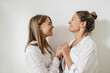 © Look! - Happy caucasian young ladies laughing looking at each other holding hands over white background. Blonde women wear shirts at home. People emotions, lifestyle concept