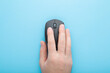 © fotoduets - Young adult man hand using dark black computer optical mouse on light blue table background. Pastel color. Closeup. Top down view.