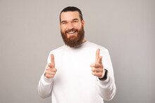 Smiling Young Man Is Pointing Towards The Camera For You In A Studio Over Grey Backdrop.