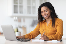 Cheerful Pretty Black Lady Working From Home, Taking Notes