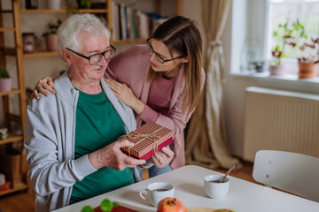 Wall Mural - Happy woman surprising her senior father when visiting him at home and bringing present.