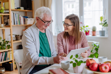 Wall Mural - Adult daughter visiting her senior father at home and using tablet.