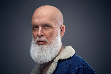 Headshot of bearded senior man with bald head dressed in warm jacket looking at camera.