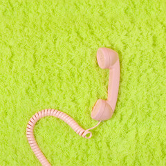 Wall Mural - Pastel pink retro telephone handset on neon  green fluffy shaggy rug background. Vintage aesthetic 80s or 90s fashion background. Romantic communication idea.