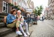 Leinwanddruck Bild - Happy senior couple tourists sitting on stairs and having take away coffee outdoors in town