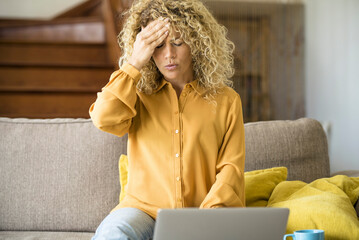 Overwork and stress bad health condition. Adult woman touching his front and head with pain. Tired and worried female people using laptop computer at home sitting ont he sofa. Stock market fall down