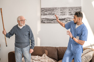 Angry elderly person threatening his caregiver with his cane