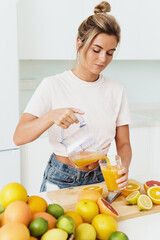 Wall Mural - Woman pouring freshly squeezed homemade orange juice into the glass in modern white kitchen