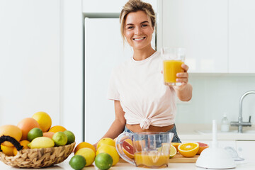 Wall Mural - Young cheerful woman with big glass of fresh orange juice