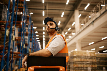 Wall Mural - Warehouse worker driving forklift while working at storage compartment.