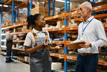 Mature Warehouse Manager And Black Female Worker Talk At Distribution Warehouse.