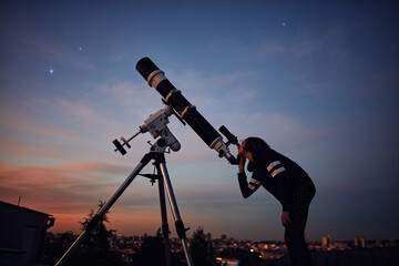 Wall Mural - girl with astronomical telescope stargazing under twilight sky.