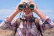 © luciano - Close up on active senior man  in outdoors excursion at sea using binoculars looking at camera, elderly caucasian male enjoying freedom and healthy lifestyle