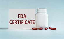 White Card With Text FDA CERTIFICATE Standing Near A Bottle Of Pills On Light Blue Background. Medical Concept.