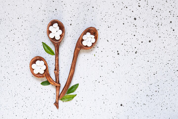 Wall Mural - Natural herbal medicine concept. Wooden spoons with natural medical capsules and tablets on white marble background with fresh green leaves top view, copy space for your text.