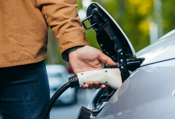 Man holding power supply cable at electric vehicle charging station. Close-up	
