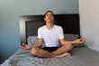 © Antonio Tanaka - Hispanic non binary long-haired man doing yoga and meditating on his bed