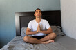 © Antonio Tanaka - Hispanic non binary long-haired man doing yoga and meditating on his bed