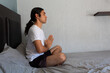 © Antonio Tanaka - Hispanic non binary long-haired man doing yoga and meditating on his bed