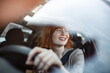 Beautiful smiling young redhead woman behind steering wheel driving car.