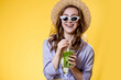 Girl in summer outfit wearing white trendy sunglasses and enjoying while drinking a Mojito cocktail. Posing on the yellow background.