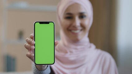Portrait smiling arabian lebanese girl muslim islamic woman in hijab hold smartphone in front show mobile phone with green screen at camera advertise app service website digital device advertisement