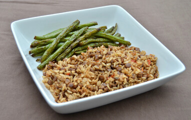 A Vegetarian Plate of Food of Brown Rice and Lentils with Green Beans on a Brown Cloth Background.