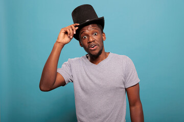 Portrait of adult with classic top hat on head in front of camera, doing magical performance with artistic prop costume in studio. Person wearing vintage costume topper for fun.