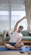© Prathankarnpap - Handsome man in sports clothes is warming up, stretching while sitting on yoga mat at home.