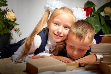 Girl and boy who is elementary school children in uniform having fun with book. Brother and sister on September 1 in Russia. Schoolgirl and schoolboy relax together. Photo shoot for the school holiday