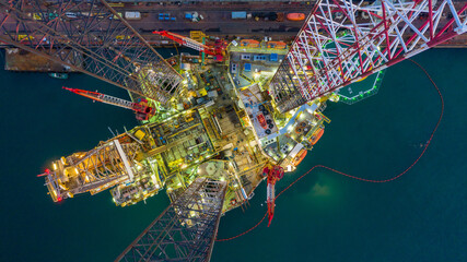 Wall Mural - Aerial top view jack up rig under maintenance at night with blue ocean, Aerial view jack up rig with towing vessel during towing operation, Offshore vessel in floating dock jack up rig under repairs.