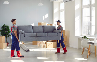 Loading service. Male loaders take sofa out of apartment while fulfilling order at moving service. Two young and strong men in overalls carry furniture. Delivery and relocation service concept.